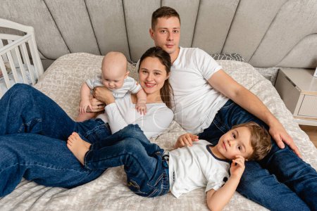 Photo for Young, emotional, cheerful, big family, mom, dad and sons lie on a big bed and look at the camera. - Royalty Free Image