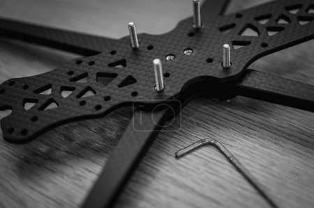 Photo for Black and white photo, background, top view, twisting drone frame parts, soldering, assembly, fpv drone part assembled by man on wooden background. Close-up, high technology, drones - Royalty Free Image