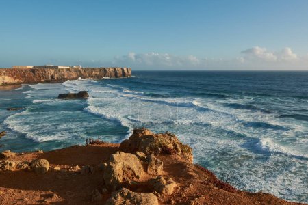 Photo for View of the beach Praia do Tonel with big waves and Sagres Fortress in the background. Sagres, Algarve region, Portugal - Royalty Free Image