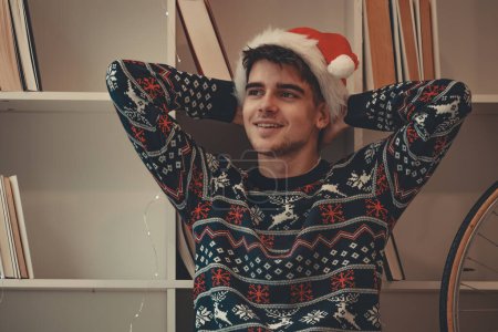 Photo for Young man at home relaxed with christmas sweater and santa claus hat - Royalty Free Image