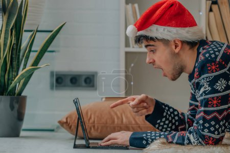 Foto de Joven en Navidad en casa con ordenador y expresión de sorpresa - Imagen libre de derechos