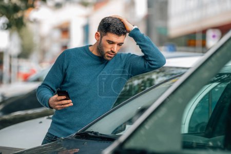 Foto de Hombre con teléfono móvil en la concesionaria mirando a los coches para comprar con expresión sorprendida - Imagen libre de derechos