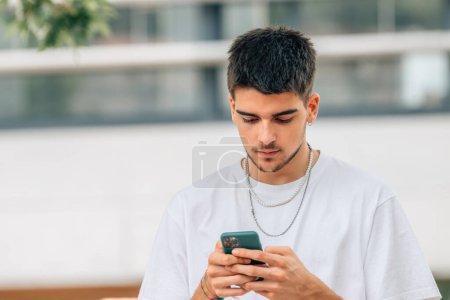 Téléchargez les photos : Young man looking at mobile phone in the street - en image libre de droit