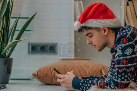 Photo for Young man with computer and mobile phone at home in christmas with santa claus hat - Royalty Free Image