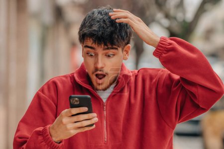 young man with mobile phone in the street with surprised expression