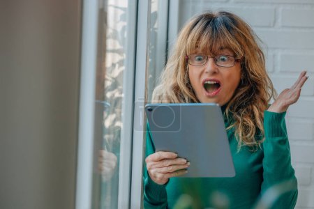 Photo for Middle aged woman with digital tablet looking surprised - Royalty Free Image