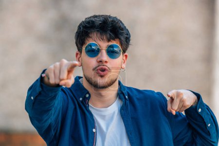 Téléchargez les photos : Young man with sunglasses in the street with expression of motivation - en image libre de droit
