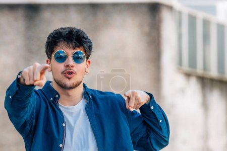 Téléchargez les photos : Young man with sunglasses in the street with expression of motivation - en image libre de droit