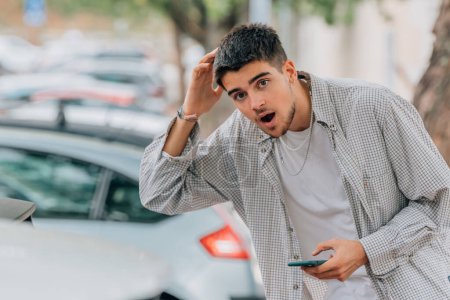 Photo for Young man on the street looking at cars with mobile phone - Royalty Free Image