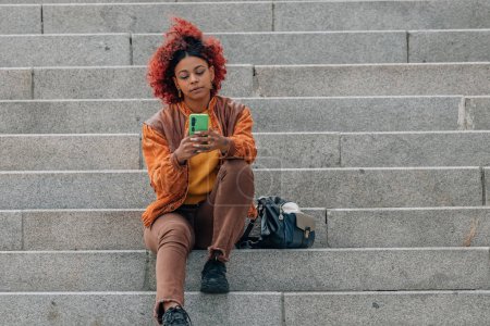 Téléchargez les photos : Afro américaine fille dans les escaliers dans la rue avec téléphone mobile - en image libre de droit