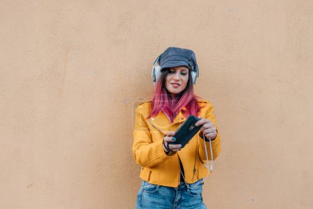 Téléchargez les photos : Fille urbaine avec téléphone portable et écouteurs isolés sur le mur de la rue - en image libre de droit