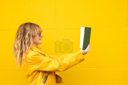 Téléchargez les photos : Femme avec manuel sur fond de mur jaune - en image libre de droit