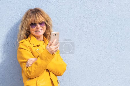 Téléchargez les photos : Femme d'âge moyen avec téléphone portable isolé sur le mur de la rue avec copie-espace - en image libre de droit