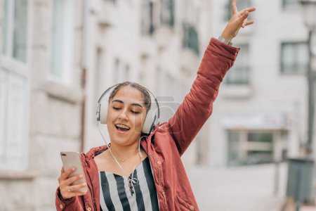 girl with mobile phone and headphones dancing on the street