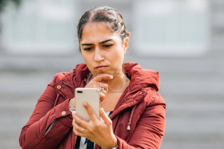 Nachdenkliches Mädchen schaut auf der Straße auf Handy