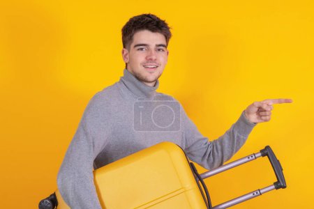 Téléchargez les photos : Jeune homme isolé avec une valise de voyage pointant - en image libre de droit