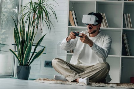 Téléchargez les photos : Jeune homme à la maison avec lunettes de réalité virtuelle et joystick - en image libre de droit