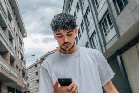 Téléchargez les photos : Jeune homme dans la rue regardant le téléphone mobile ou smartphone - en image libre de droit