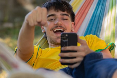 Foto de Macho joven en la hamaca con el teléfono móvil que celebra excitado para la alegría - Imagen libre de derechos