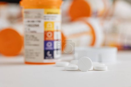 Ein Bündel verschreibungspflichtiger Tablettenflaschen gruppiert auf einem Tisch mit weißem Hintergrund und Tabletten heraus