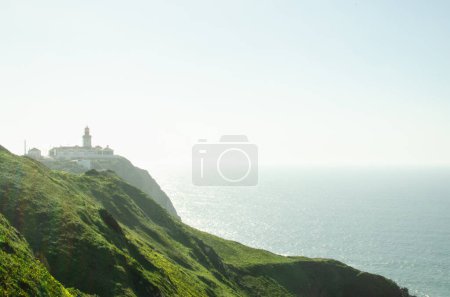 Photo for Cabo da Roca cape view on the lighthouse, green hills with yellow flowers ocean blue sky landscape scenic travel photography contra light portugal - Royalty Free Image