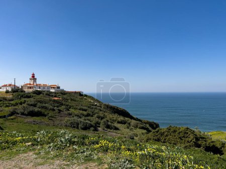 Photo for Cabo da Roca cape view on the lighthouse, green hills with yellow flowers ocean blue sky landscape scenic travel photography contra light portugal - Royalty Free Image