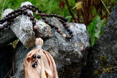 Handmade mala necklace with wooden beads and silk tassel resting on grey stones. 