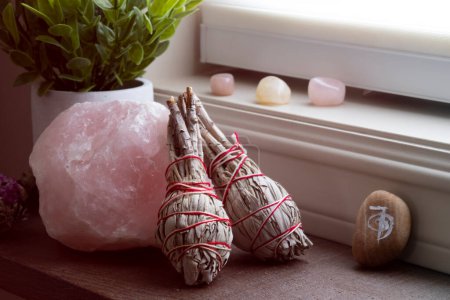 Foto de A close up image of a large raw piece of rose quartz with two white sage smudge sticks. - Imagen libre de derechos