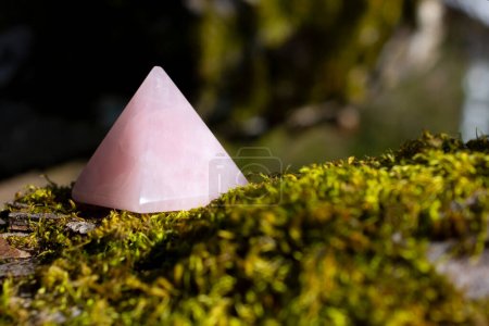 A close up image of a rose quartz crystal pyramid on a bright green patch of thick moss. 