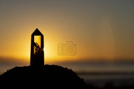 A beautiful peaceful image of a smoky quartz crystal tower against the backdrop of a bright golden sunset. 