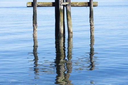 An image of the rippled water reflection of old dock pilings left behind to decay in the blue ocean water. 