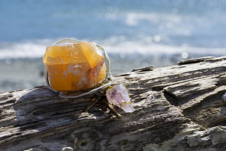 Foto de Una imagen de un gran cristal de calcita naranja con péndulo hecho a mano descansando sobre una vieja pieza de madera a la deriva con un fondo azul océano. - Imagen libre de derechos