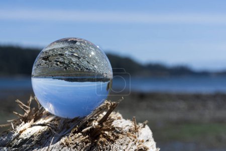 An close up image of a crystal clear photographic lens ball with the Pacific Ocean in the background. 