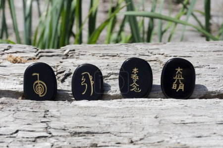 Une image rapprochée de quatre cristaux de tourmaline noirs avec des symboles de guérison reiki écrits sur eux.