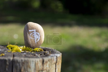 Image d'un symbole guérisseur Reiki peint sur une pierre beige et reposant sur un poteau de clôture recouvert de mousse. 