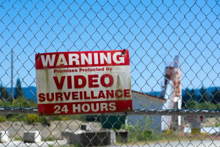Une image rapprochée d'un très vieux panneau d'avertissement de vidéosurveillance affiché sur une barrière à maillons de chaîne verrouillés. 