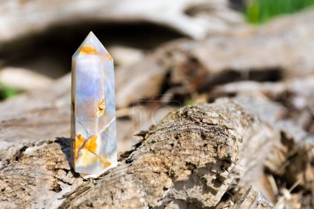 A close up image of blue agate crystal healing tower with flower inclusions resting on a rough driftwood log. 