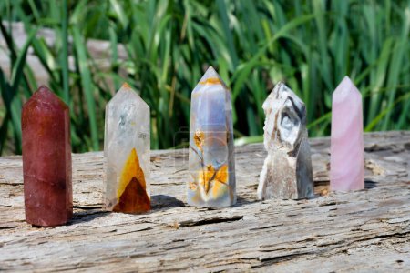An image of five healing crystal towers lined up on an old weathered log. 