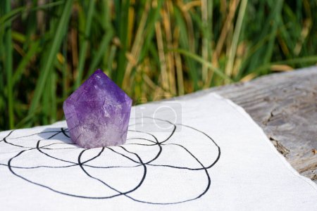 An image of a large purple amethyst crystal tower on a grid cloth with the flower of life pattern. 