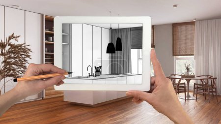 Hands holding and drawing on tablet showing minimal white and wooden kitchen details CAD sketch. Real finished interior in the background, architecture design presentation