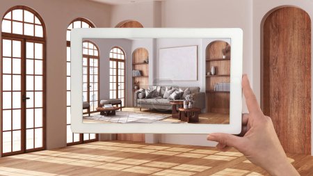 Augmented reality concept. Hand holding tablet with AR application used to simulate furniture and design products in empty interior with parquet floor, farmhouse living room