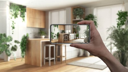 Hand holding smart phone, AR application, simulate furniture and interior design products in real home, architect designer concept, blur background, modern wooden kitchen