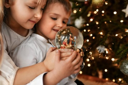 Photo for The kids looking at a glass ball with a nativity scene of the birth of Jesus Christ - Royalty Free Image