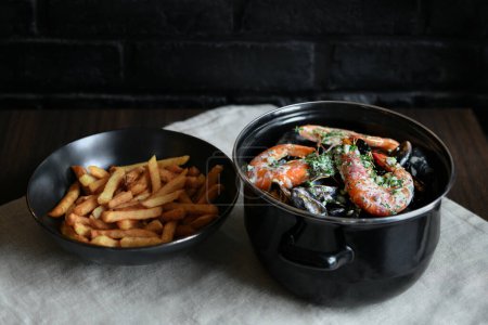 Téléchargez les photos : Moules avec sauce et crevettes et frites sur fond noir - en image libre de droit