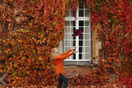 Foto de Mujer en un suéter naranja cerca de una pared con uvas silvestres en otoño - Imagen libre de derechos