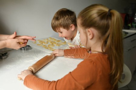 Téléchargez les photos : Frère et sœur déroulant la pâte à biscuits lapin pour Pâques à la cuisine - en image libre de droit