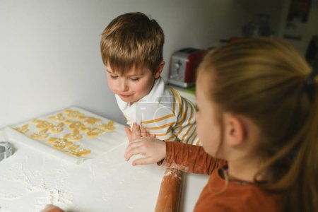 Téléchargez les photos : Frère et sœur déroulant la pâte à biscuits lapin pour Pâques à la cuisine - en image libre de droit