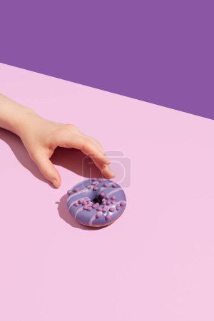 Téléchargez les photos : Une main avec un donut savoureux sur un fond de couleur - en image libre de droit
