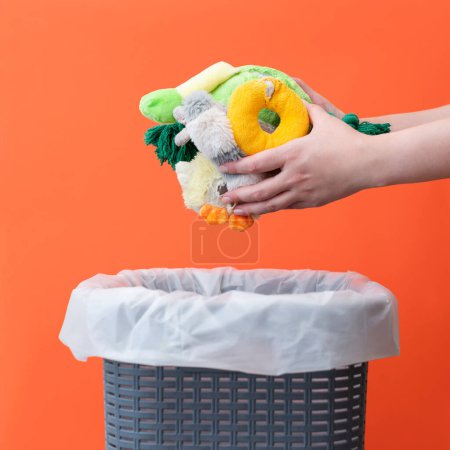 Foto de Mujer poniendo los juguetes rotos en un cubo de basura sobre un fondo naranja, espacio para copiar - Imagen libre de derechos
