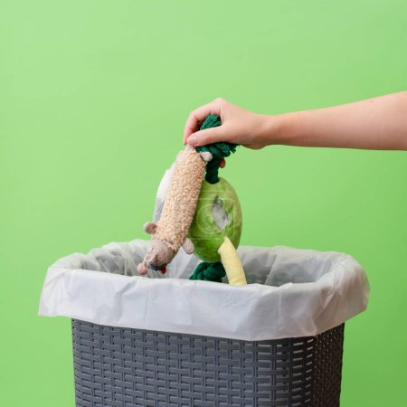 Photo for Woman putting the broken toys in waste bin on a green background, copy space - Royalty Free Image